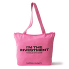 Black woman holding a pink canvas tote that reads “I’M THE INVESTMENT – HANDLE WITH CARE” by Baddies & Budgets